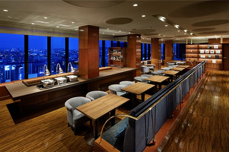 夜景を望む広々とした空間にテーブル席が並ぶラウンジ