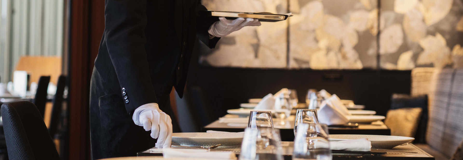 レストランスタッフがレストラン内でテーブルにカトラリーなど並べ準備をしている様子