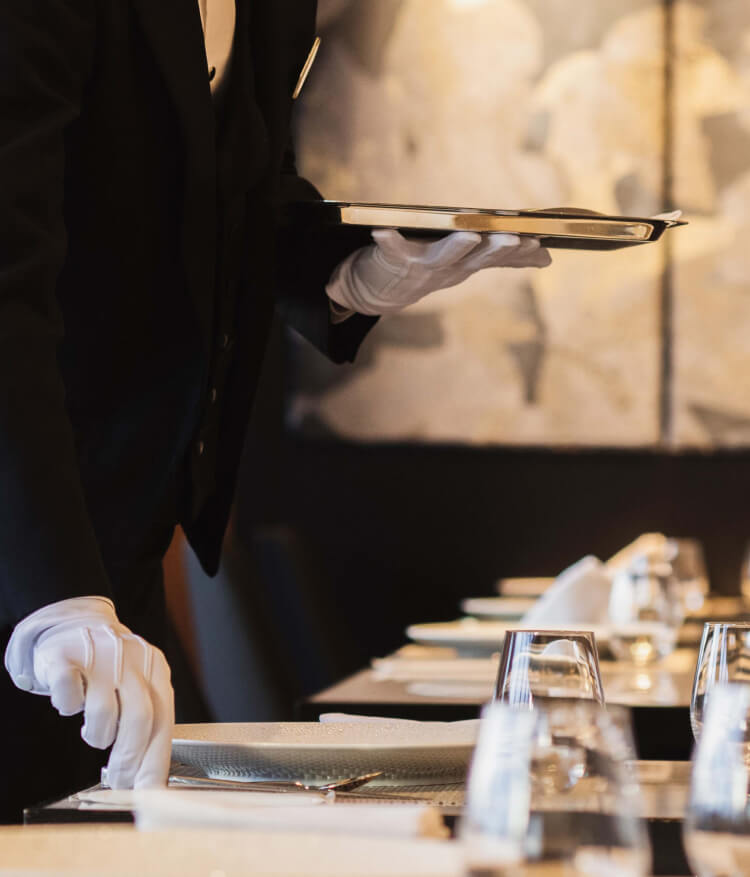レストランスタッフがレストラン内でテーブルにカトラリーなど並べ準備をしている様子