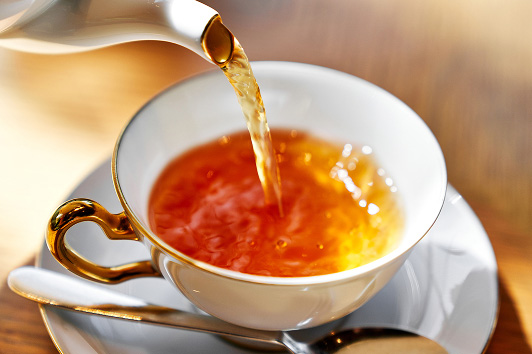 温かい紅茶がティーポットから白いティーカップに注がれている瞬間のクローズアップ。