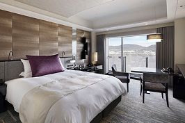 高級感あふれるホテルのツインベッドルームの全景。中央には、ふかふかの白い寝具が整えられた大きなベッドがあり、ベッドの上には紫色のクッションがアクセントとして置かれている。