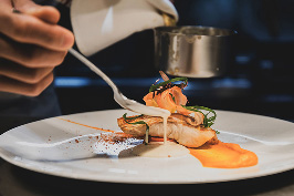 シェフが、白い皿に盛り付けられた料理の仕上げをしているクローズアップ。
