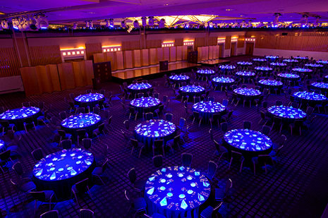 暗い照明の中、青いライトで照らされた丸テーブルが多数配置された大規模な宴会場