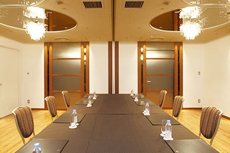 茶色と黒を基調とした内装の、黒いテーブルクロスがかけられた長テーブルが配置された役員会議室または小宴会場