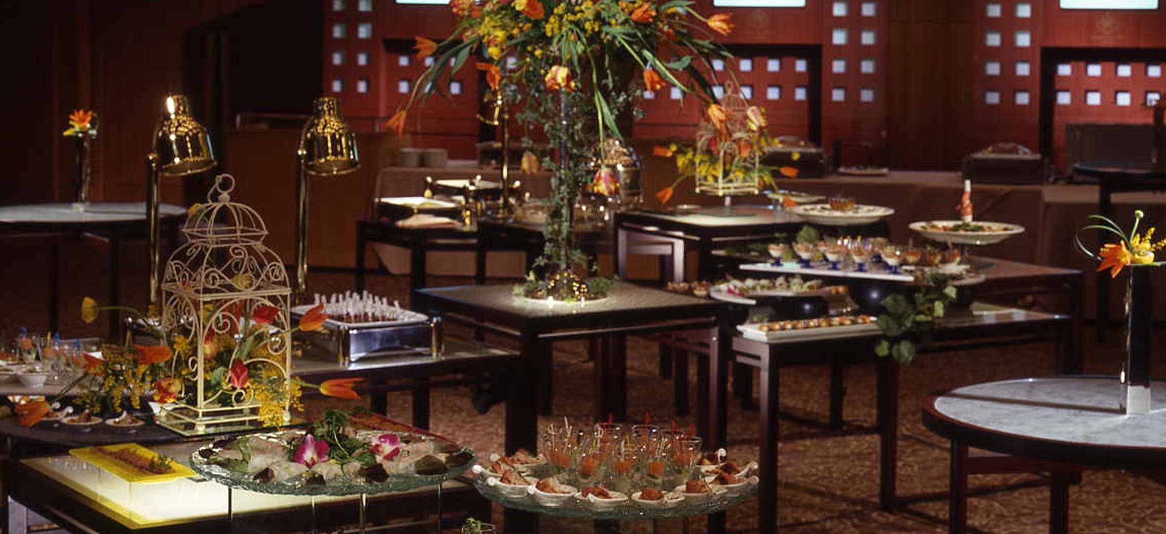 華やかな照明で彩られた広々としたイベントホールの全体像です。室内は主に紫色と青色のライトで照らされ、幻想的な雰囲気を醸し出しています。手前から奥にかけて、多数の丸いテーブルが配置されており、それぞれのテーブルには青い照明が当てられ、テーブルの表面には白い模様が浮かび上がっています。