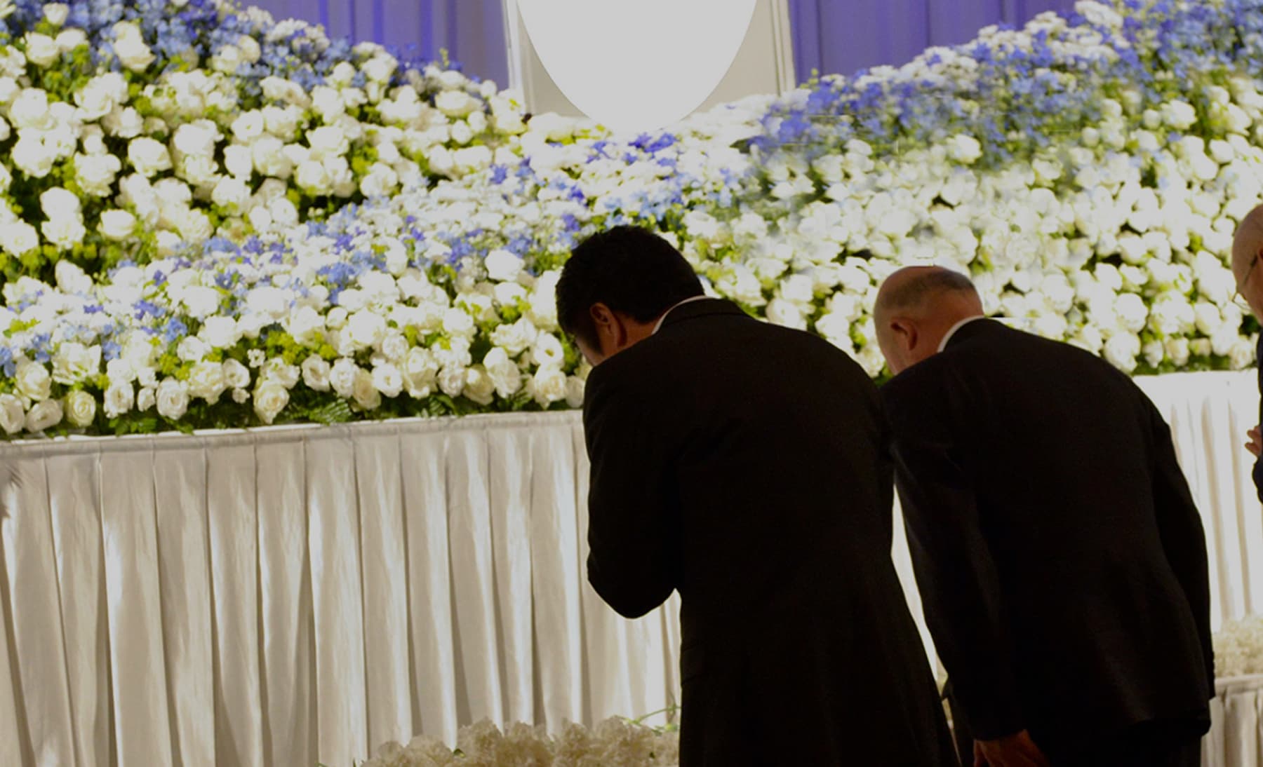 ご葬儀・お別れの会。祭壇の花に頭を下げる参列者。