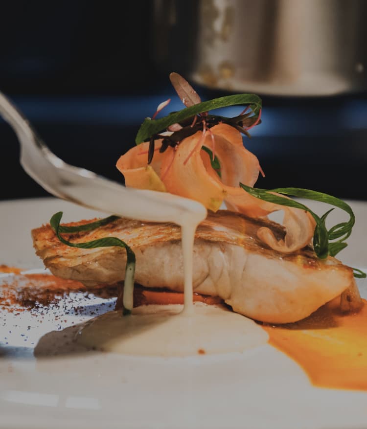シェフの手によって丁寧に仕上げられる繊細な魚料理。鮮やかなオレンジのピューレと白いソースのコントラストが美しい一皿。