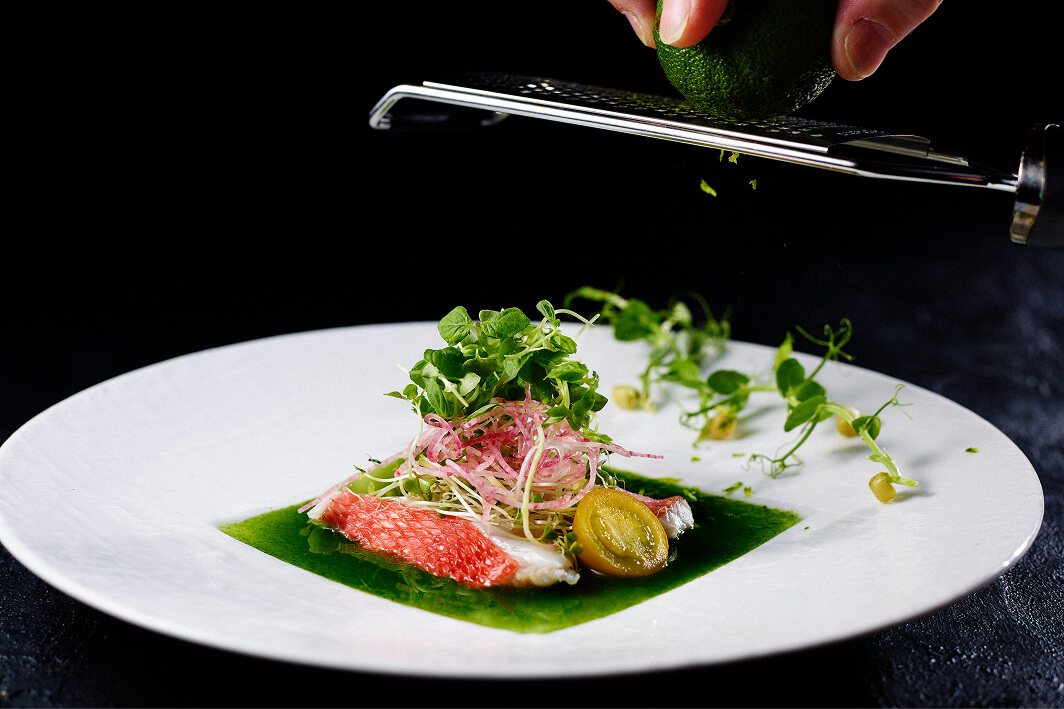 白身魚の前菜にライムの皮を削って香りを加えるシーン。美しい盛り付け。