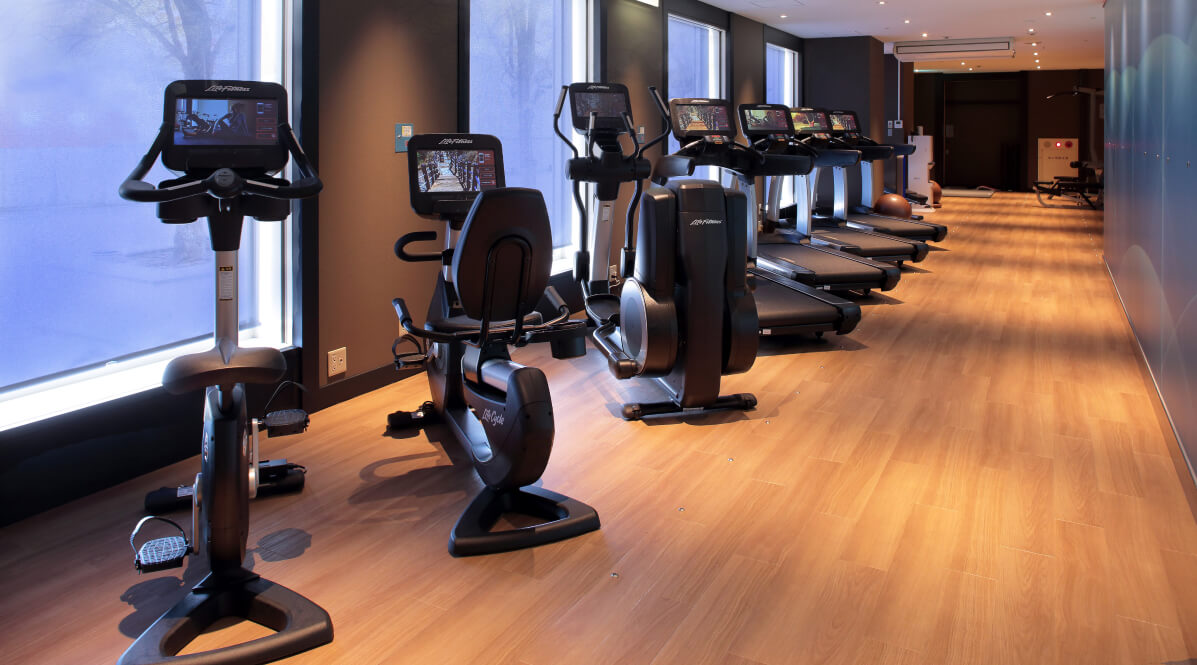 木の床が美しい開放感のあるフィットネスジムのランニングマシンエリア