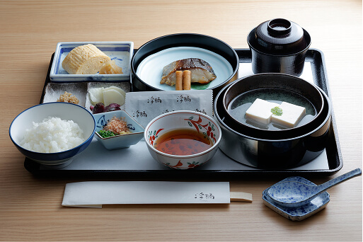 和朝食の膳。焼き魚、豆腐、玉子焼き、小鉢、ご飯、味噌汁などが整然と並んだ日本料理の朝食セット。