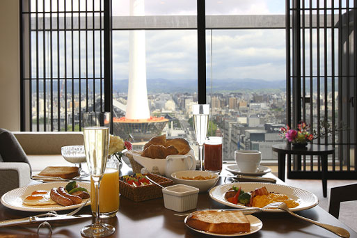 窓の外に街の景色が広がるダイニングでの朝食風景。洋朝食がテーブルに並び、明るい自然光が差し込む。