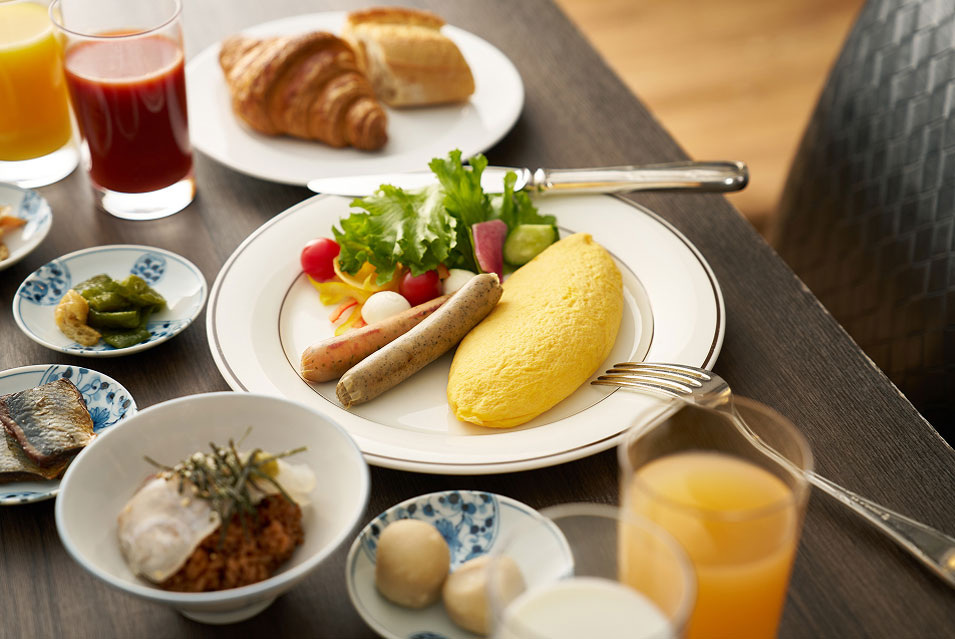 洋朝食のプレート。ふわふわのオムレツとソーセージ、サラダ、パン、ジュースなどが並ぶ。