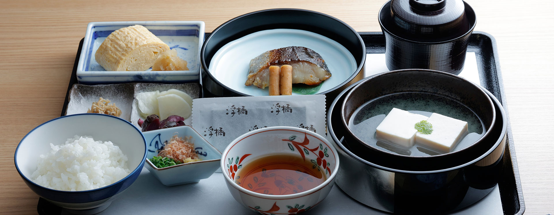 和朝食の膳。焼き魚、豆腐、玉子焼き、小鉢、ご飯、味噌汁などが整然と並んだ日本料理の朝食セット。