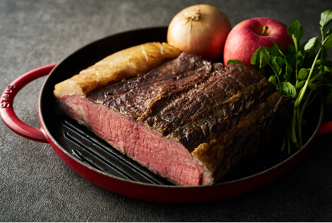 鉄鍋に盛られたローストビーフ。断面が美しく焼かれ、リンゴや野菜が添えられている。