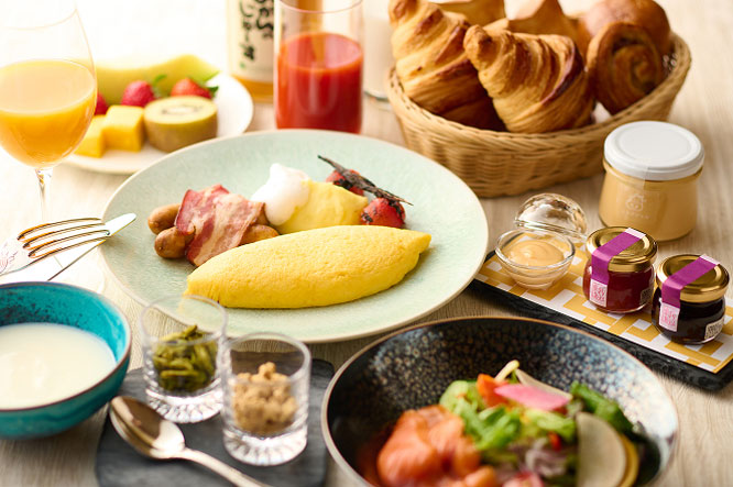 彩り豊かな洋朝食。オムレツ、サラダ、フルーツ、クロワッサン、ヨーグルト、ジュースが並んでいる。