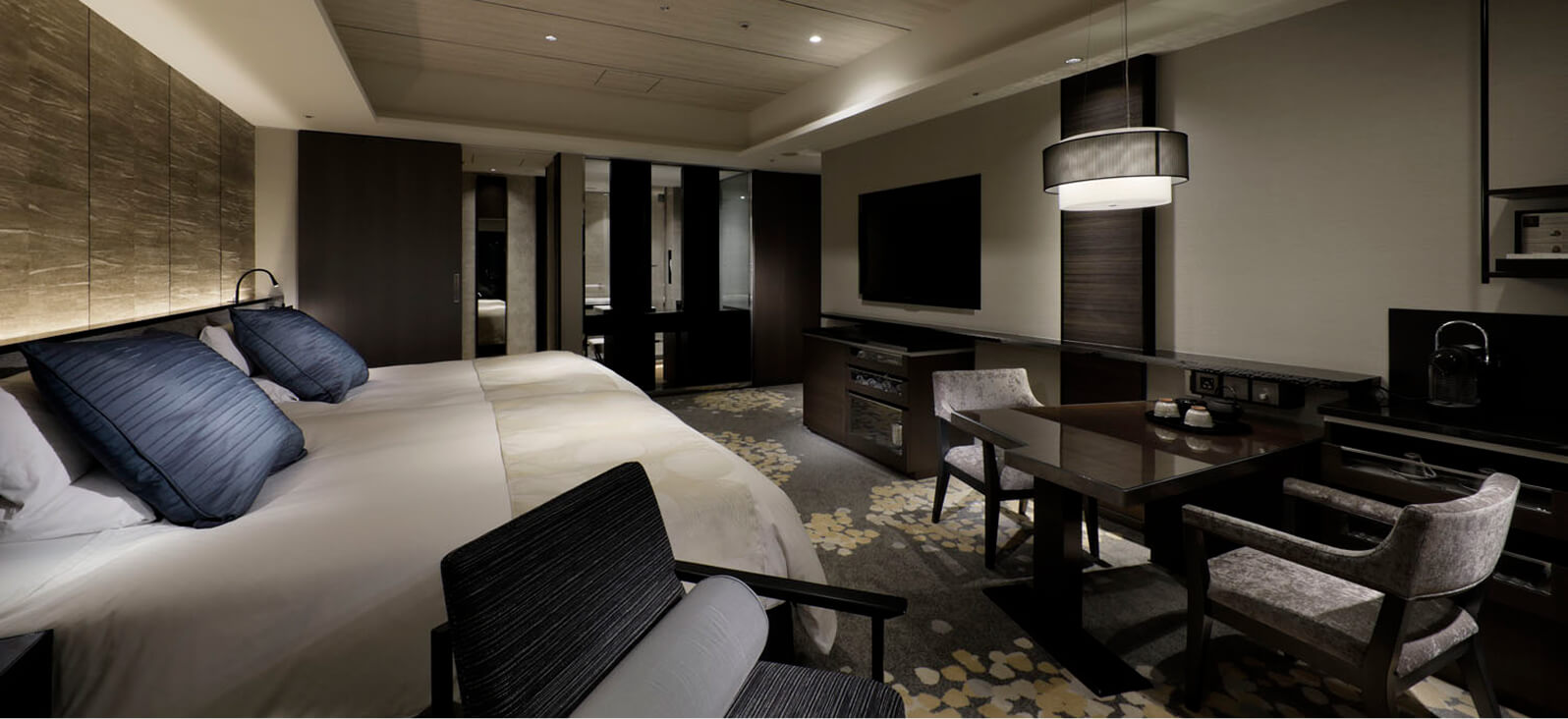 照明とソファセットが配置された、落ち着いた色合いのベッドルーム