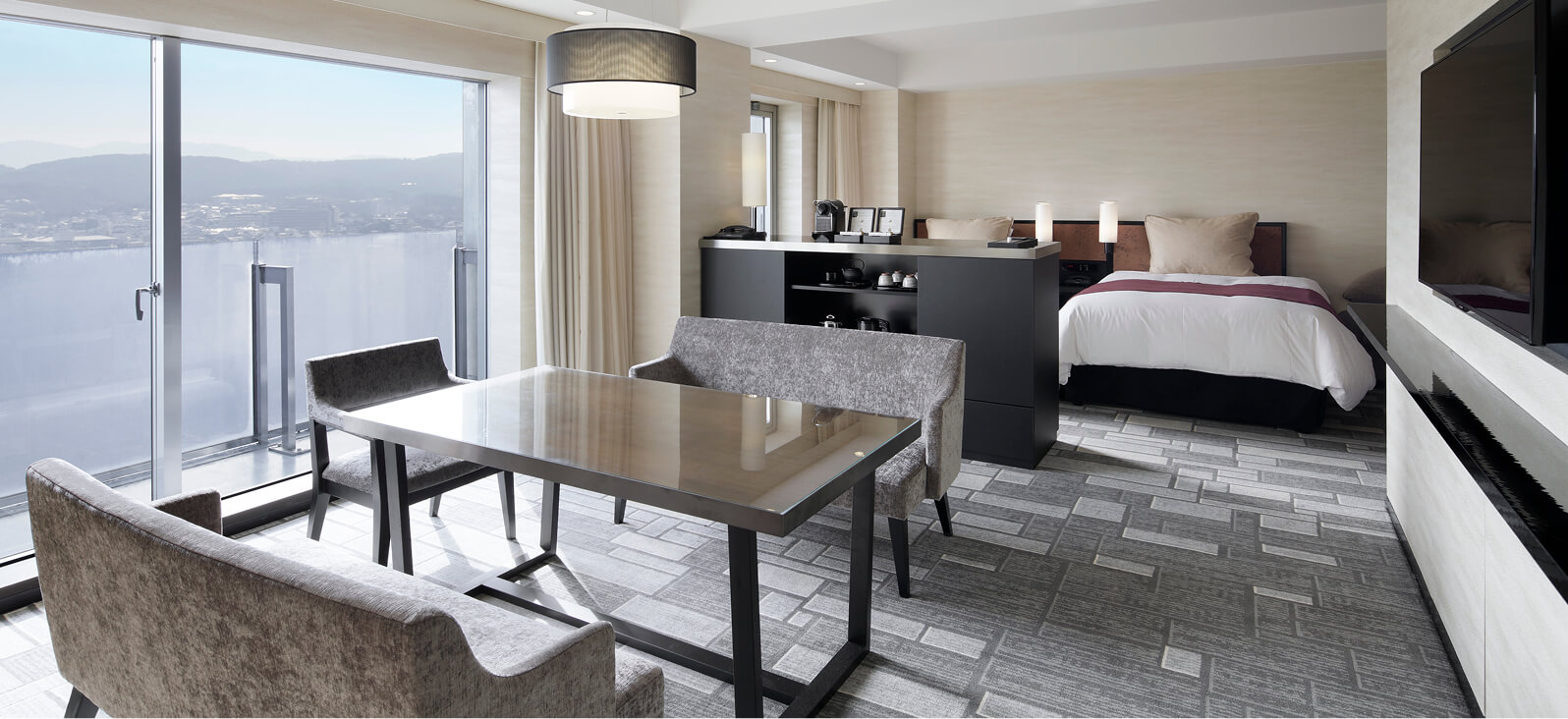 大きな窓から湖を一望できる、ダイニングテーブルとベッドが同空間にあるモダンなグランヴィアファミリールーム