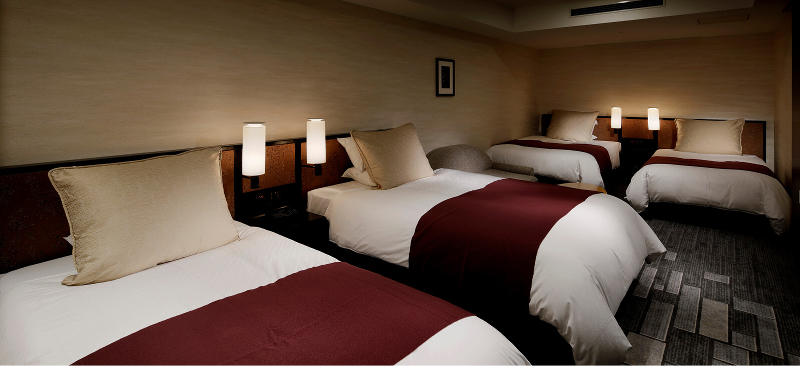 2台ずつ計4台のベッドが並ぶ、ダークな木目と暖色照明で落ち着いた雰囲気のグランヴィアファミリールーム