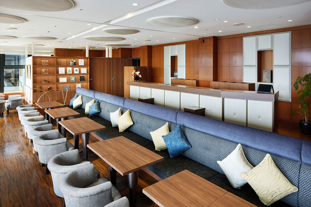 木目調の机と青や白のクッションがあり、落ち着いた雰囲気のソファ・テーブル席がならぶラウンジ