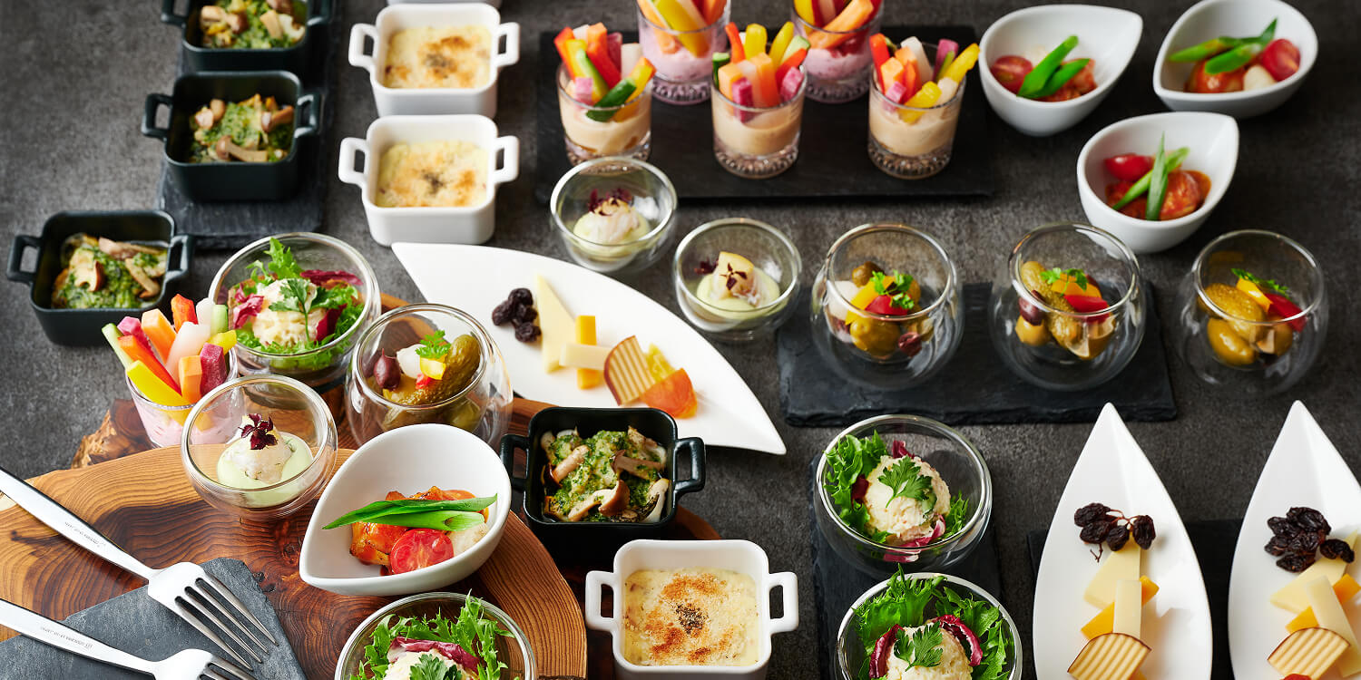 パーティーを彩る多彩なアミューズと温製料理の盛り合わせ。新鮮な野菜やチーズ、温かい小皿料理が並ぶ華やかなオードブルのイメージ。