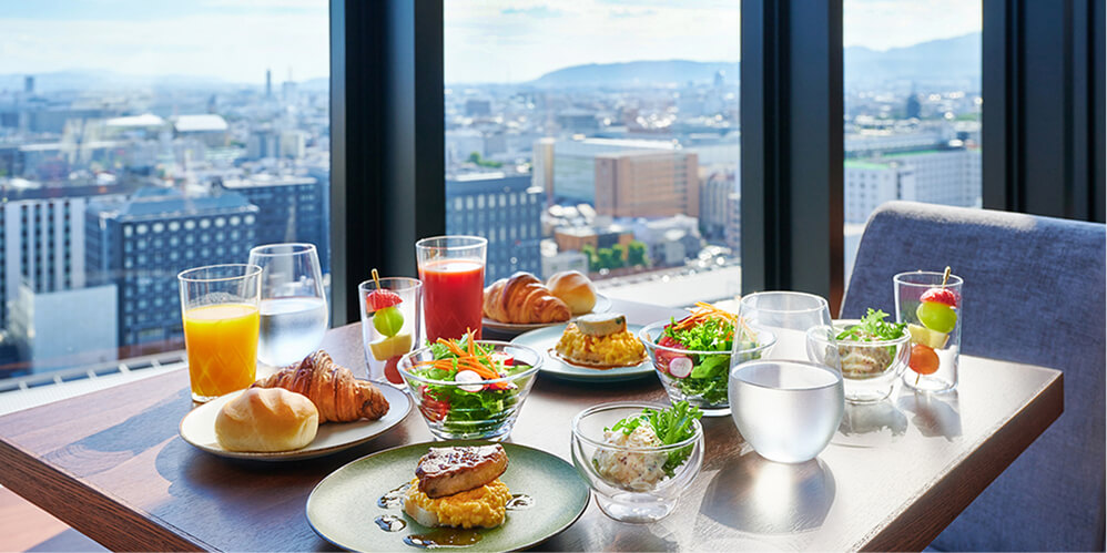 高層階の窓から街並みが見える席で提供されている、クロワッサンやサラダなどの洋食の朝食。