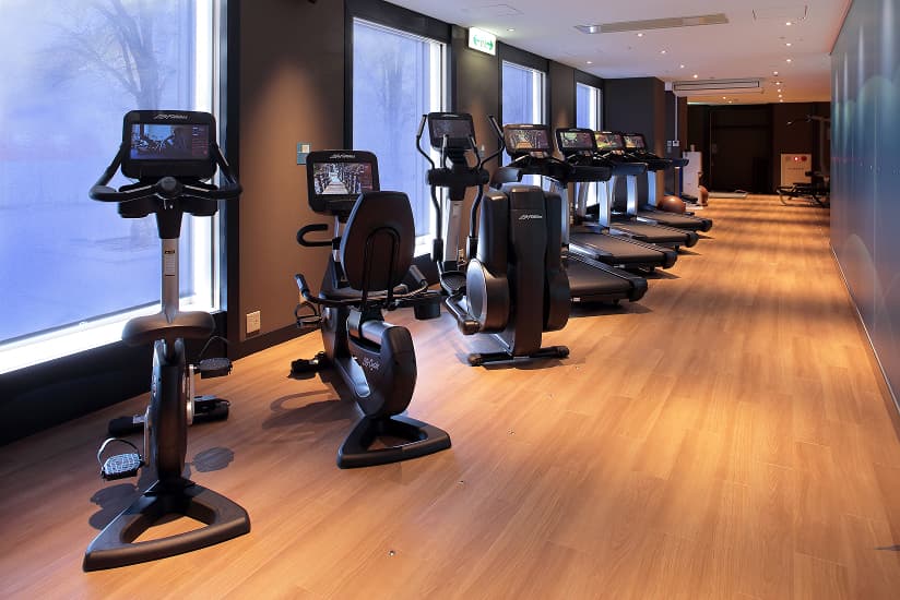 トレッドミルやバイクなどの有酸素運動マシンが並ぶ、窓のあるフィットネスジム。