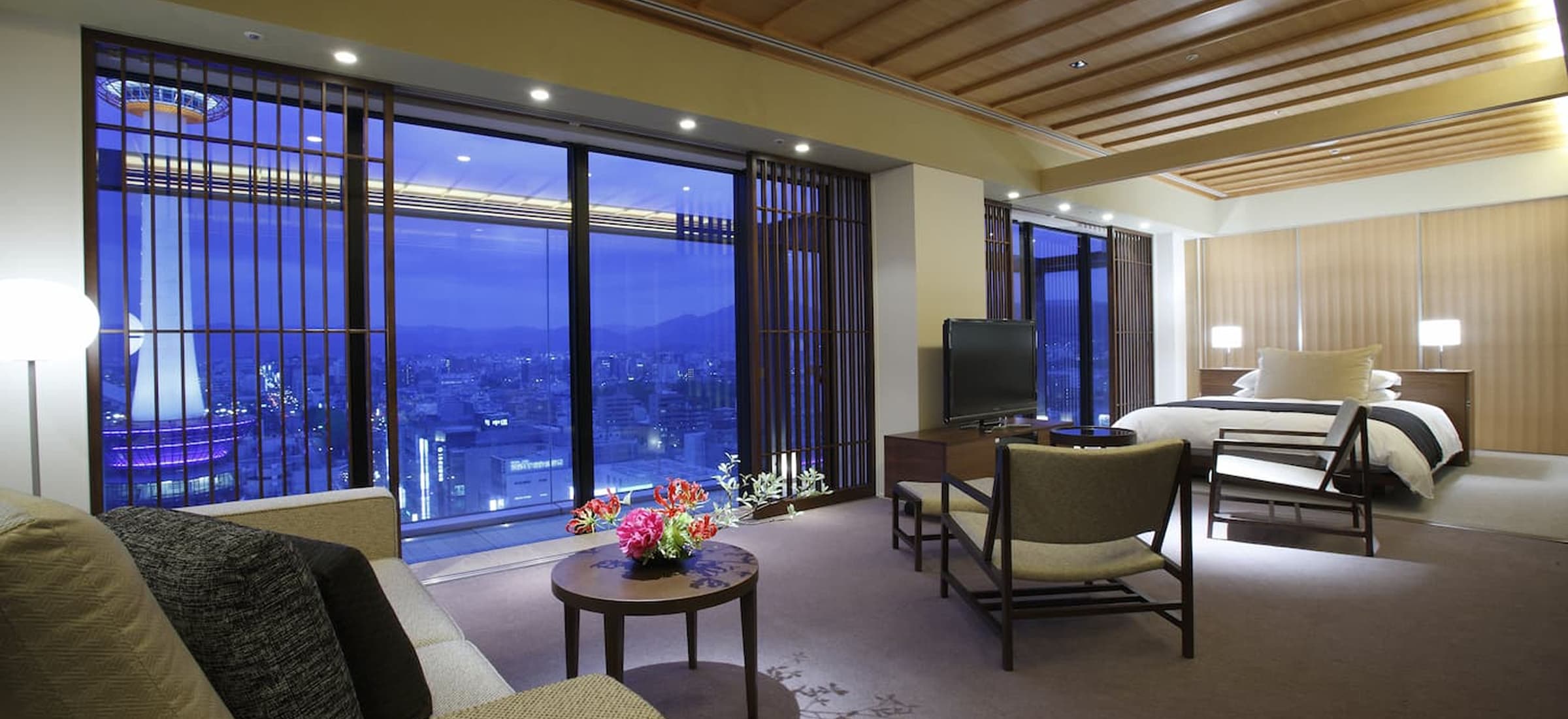 窓の外に夜景が広がる、モダンで和風な内装のホテルの客室。