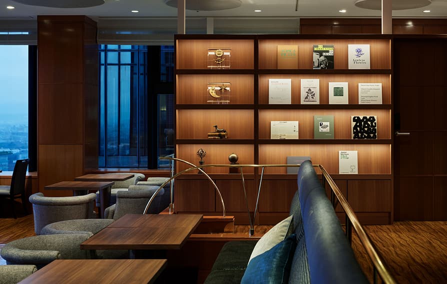 窓からの眺めが見える、棚に本や小物が飾られた落ち着いた雰囲気のラウンジ。