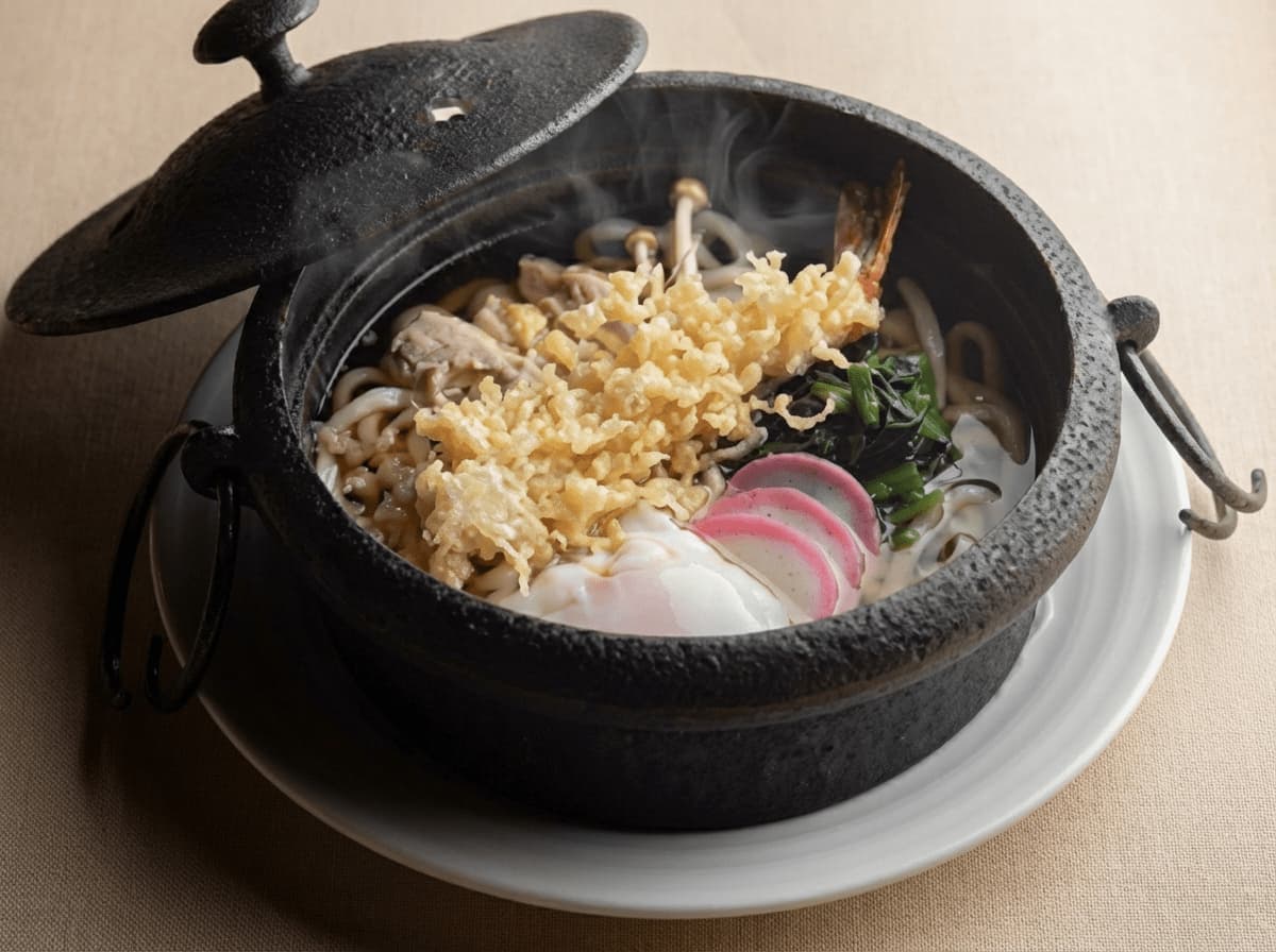 蓋付きの黒い土鍋に入ったうどん料理