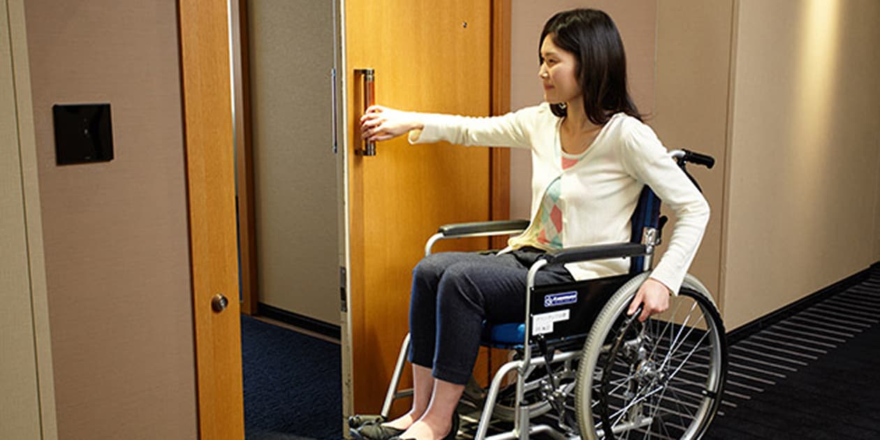 車椅子の女性がホテルの客室ドアを開けようとしている様子。