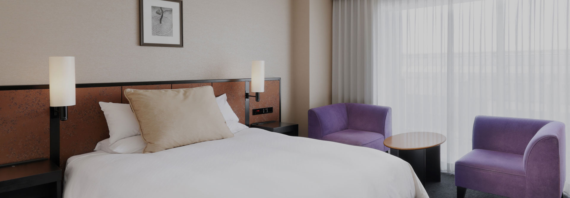 シンプルなインテリアのダブルルーム、紫のチェアが並ぶ窓辺