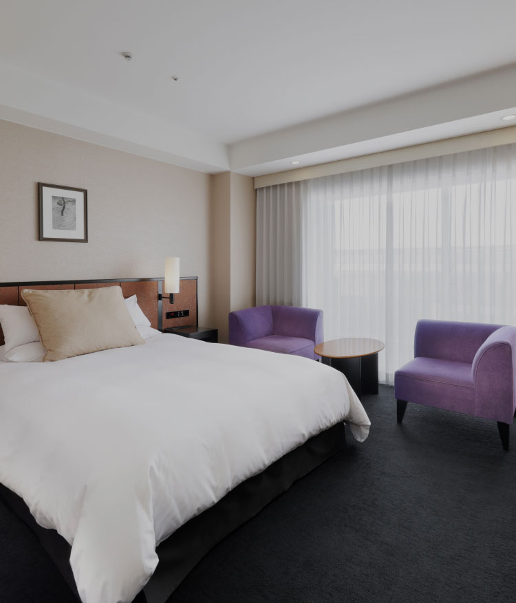 シンプルなインテリアのダブルルーム、紫のチェアが並ぶ窓辺