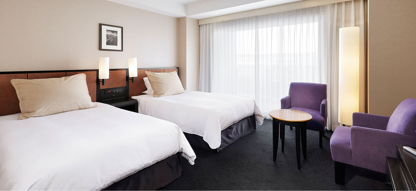 明るいツインルーム、2台のベッドと窓際の紫のチェアセット