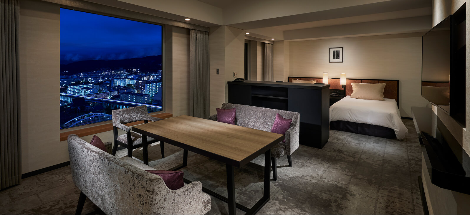 夜景を望む窓際にダイニングテーブルとソファを配置した、ベッドルーム一体型のシックな客室