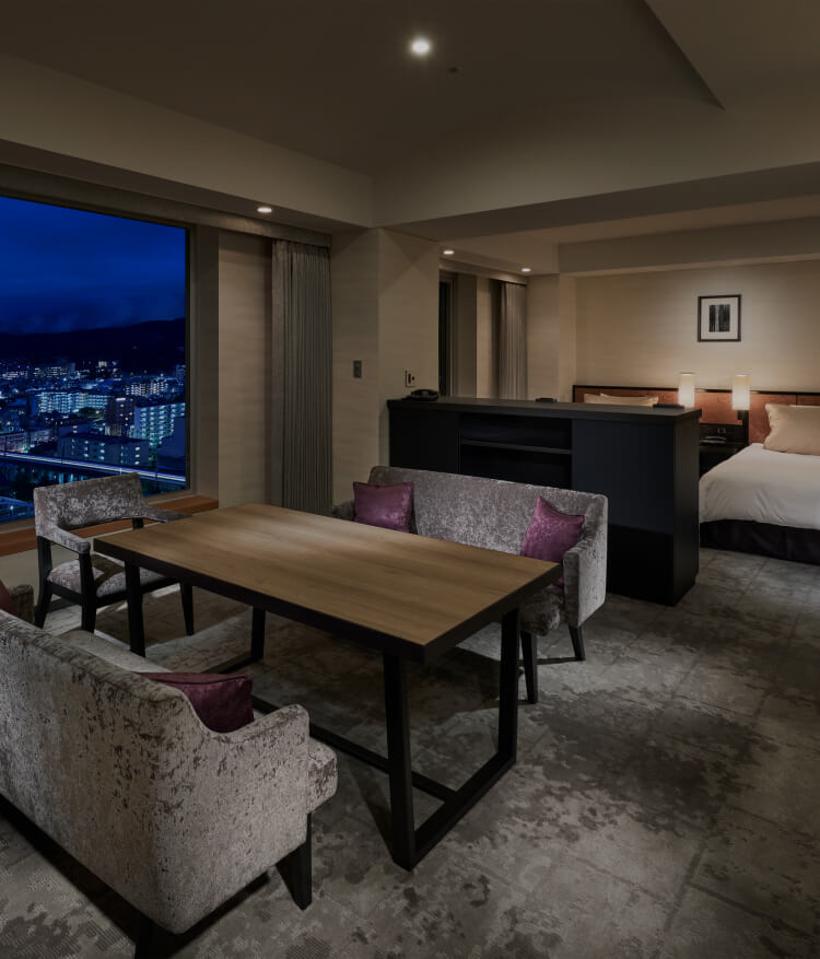 夜景を望む窓際にダイニングテーブルとソファを配置した、ベッドルーム一体型のシックな客室