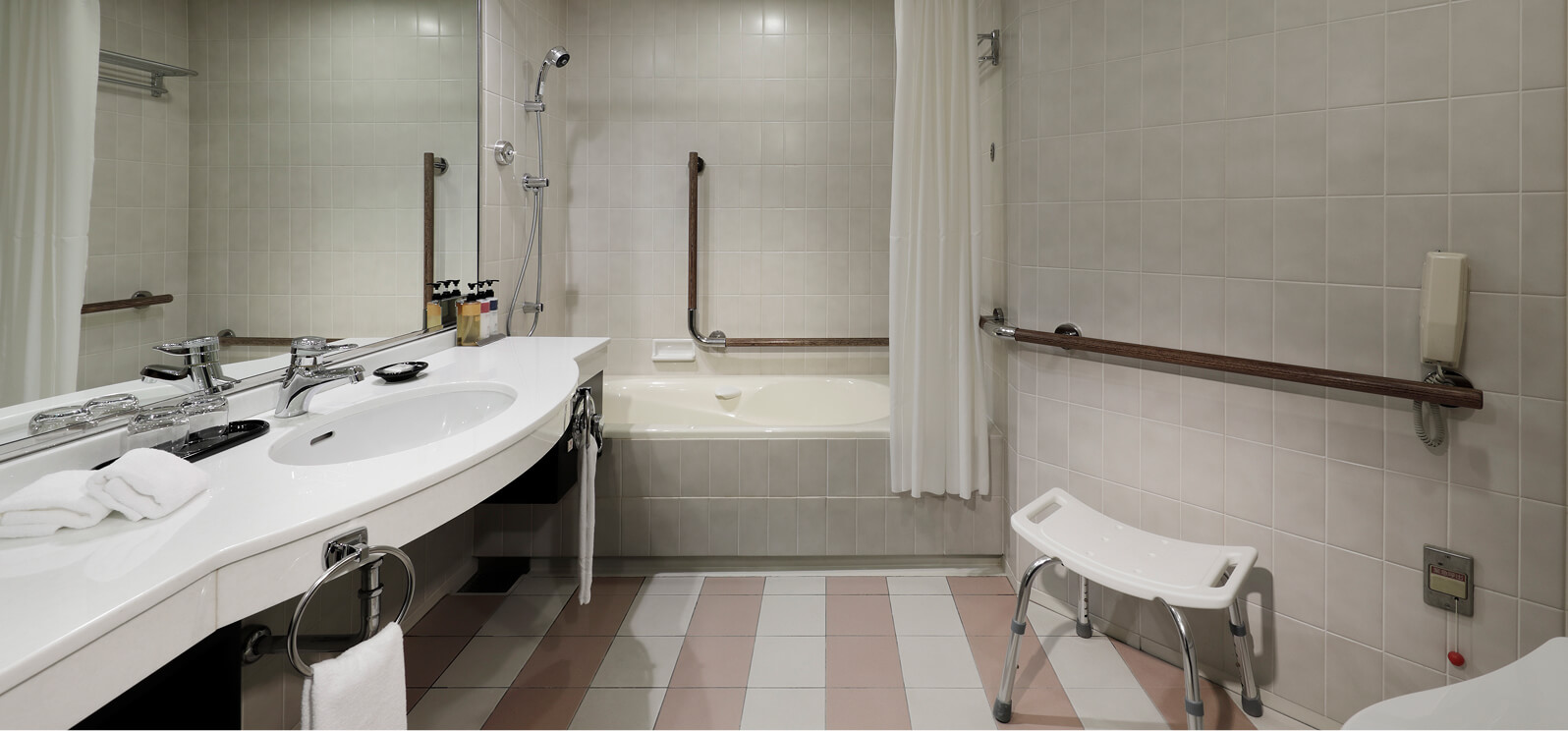 バリアフリー対応の広々とした浴室、複数の手すりと椅子を備えたユニバーサル仕様
